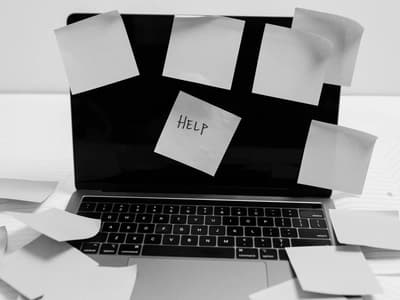 A black-and-white photo of a laptop covered in sticky notes, with "HELP" on one, symbolizing the overwhelming nature of ADHD