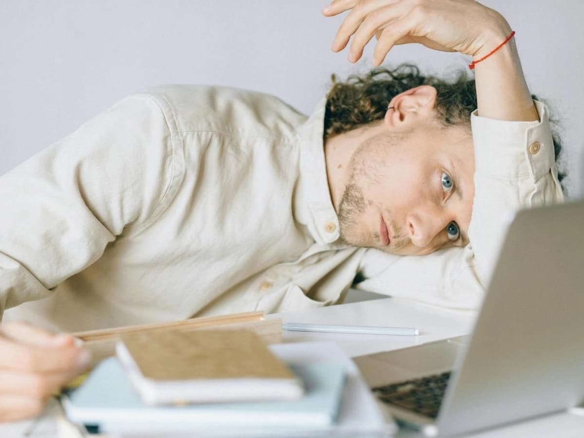A man with ADHD, overwhelmed and unable to focus, rests his head on his desk in a moment of exhaustion