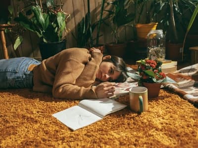 Overwhelmed woman resting on the floor with art supplies and coffee mug, representing emotional challenges linked to ADHD and hormones
