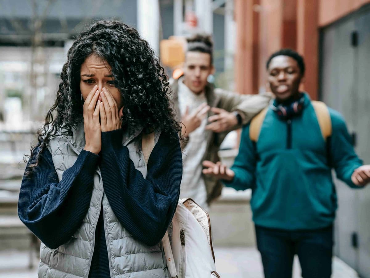 A woman hides her face in distress, with two men behind her. This depicts the emotional sensitivity and social struggles often associated with ADHD