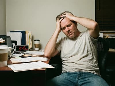 A man overwhelmed by his messy desk. Disorganization and task paralysis are stressful symptoms of adult ADHD