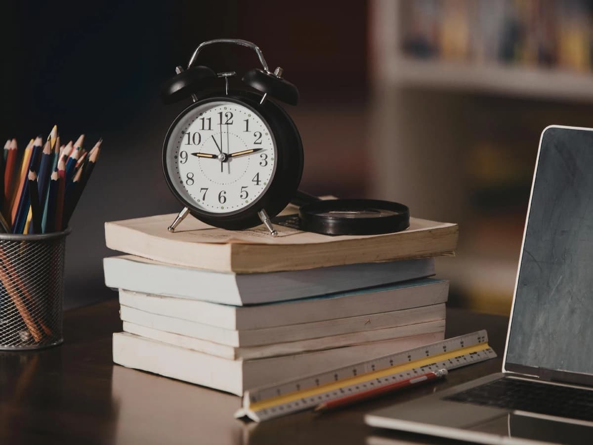 A stack of books with an alarm clock and laptop, representing time management challenges for adults managing ADHD daily