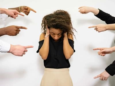 A woman covers her ears amidst pointing fingers, depicting the sensory overload and emotional sensitivity often experienced by those with ADHD